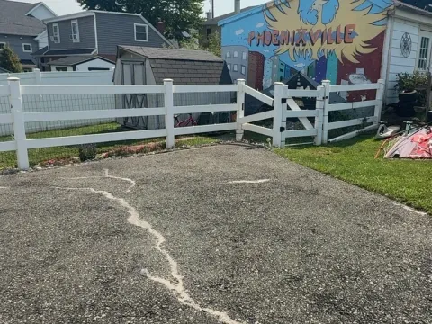 Cracked residential driveway before sealcoating, garage with Phoenixville mural in background